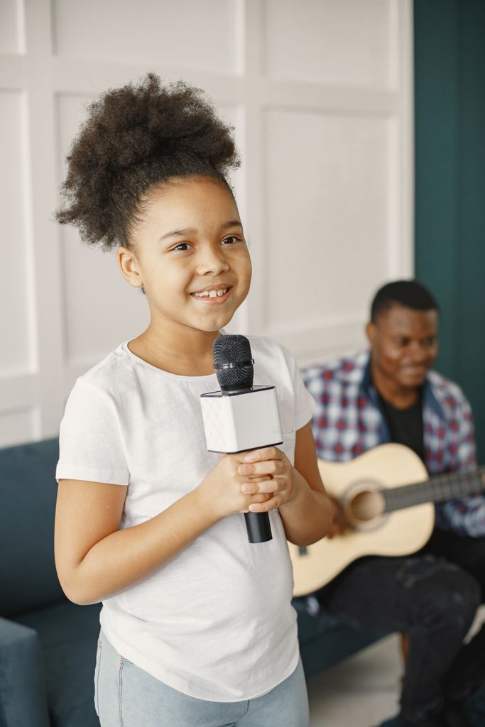 Smiling girl holding a microphone with a guitarist in the background, creating a harmonious musical moment.