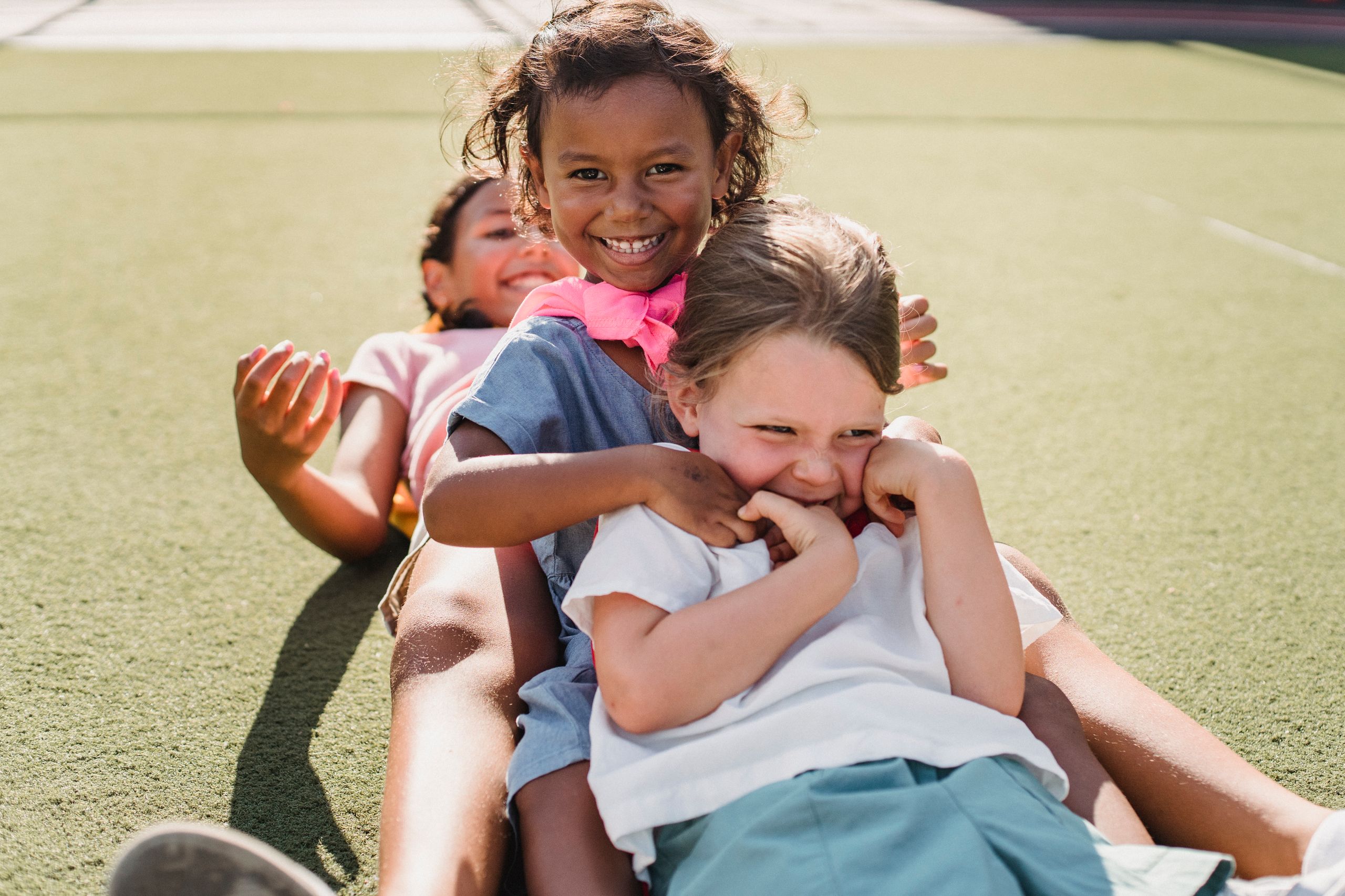 Three smiling children playfully enjoying the sunshine outdoors, showcasing friendship and fun.